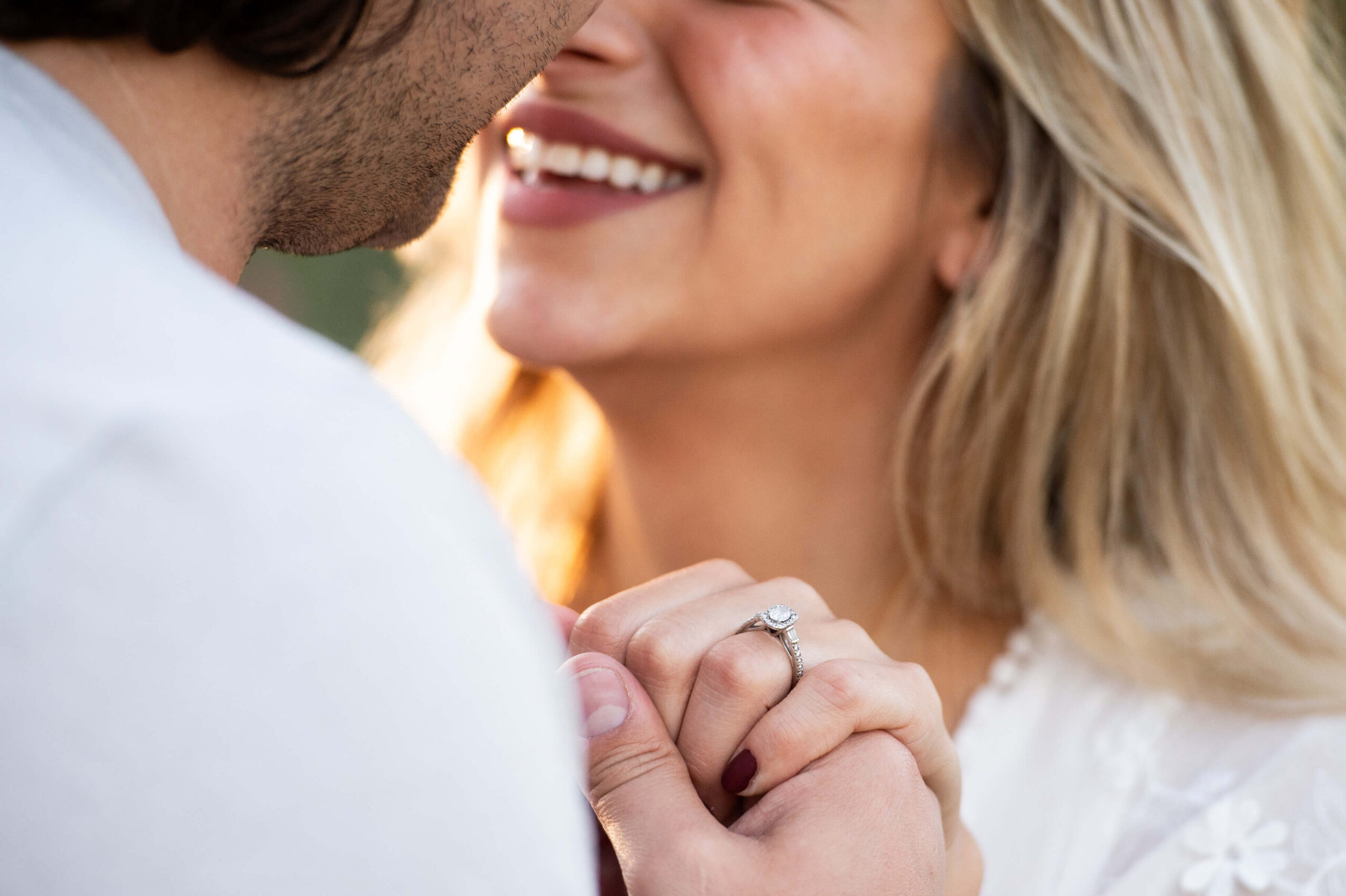 a closeup photo of an engagement ring with a female smiling in the background. Captured by JEMMAN Photography