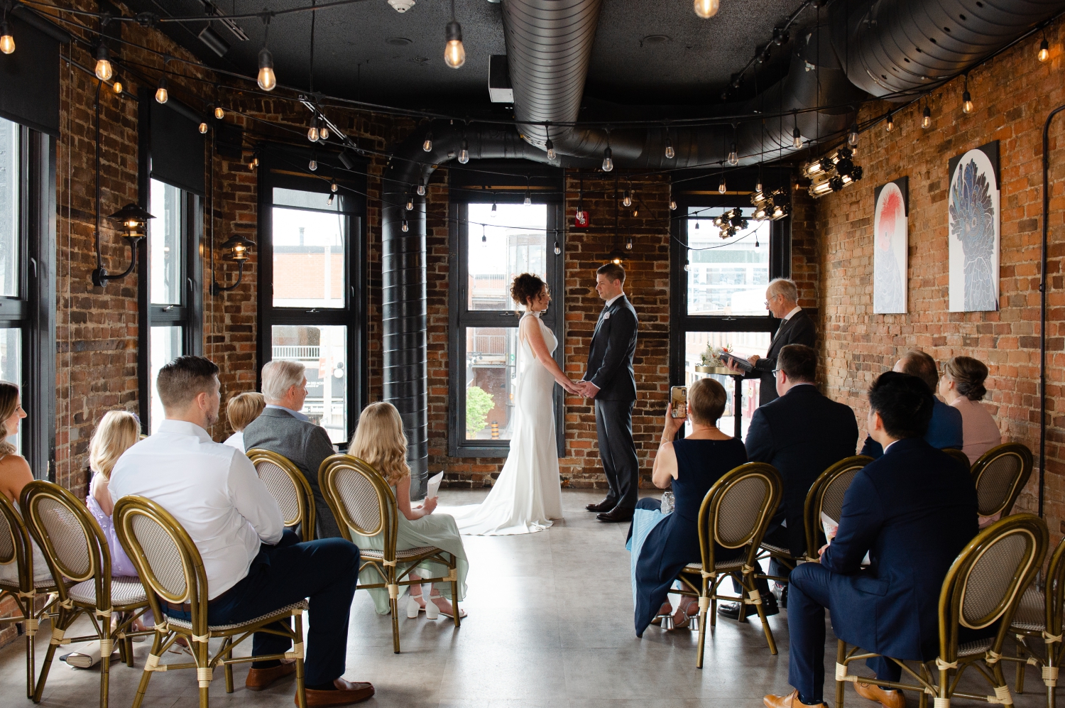 a bride and groom holding hands during their Starling Ottawa wedding ceremony while their guests look on. Captured by JEMMAN Photography