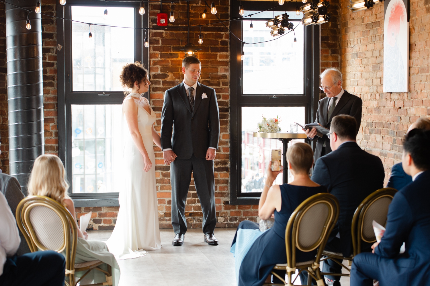 a bride and groom holding hands listening as their officiant, Jim Emerson, leads their wedding ceremony in the private room of the Starling restaurant. Captured by JEMMAN Photography