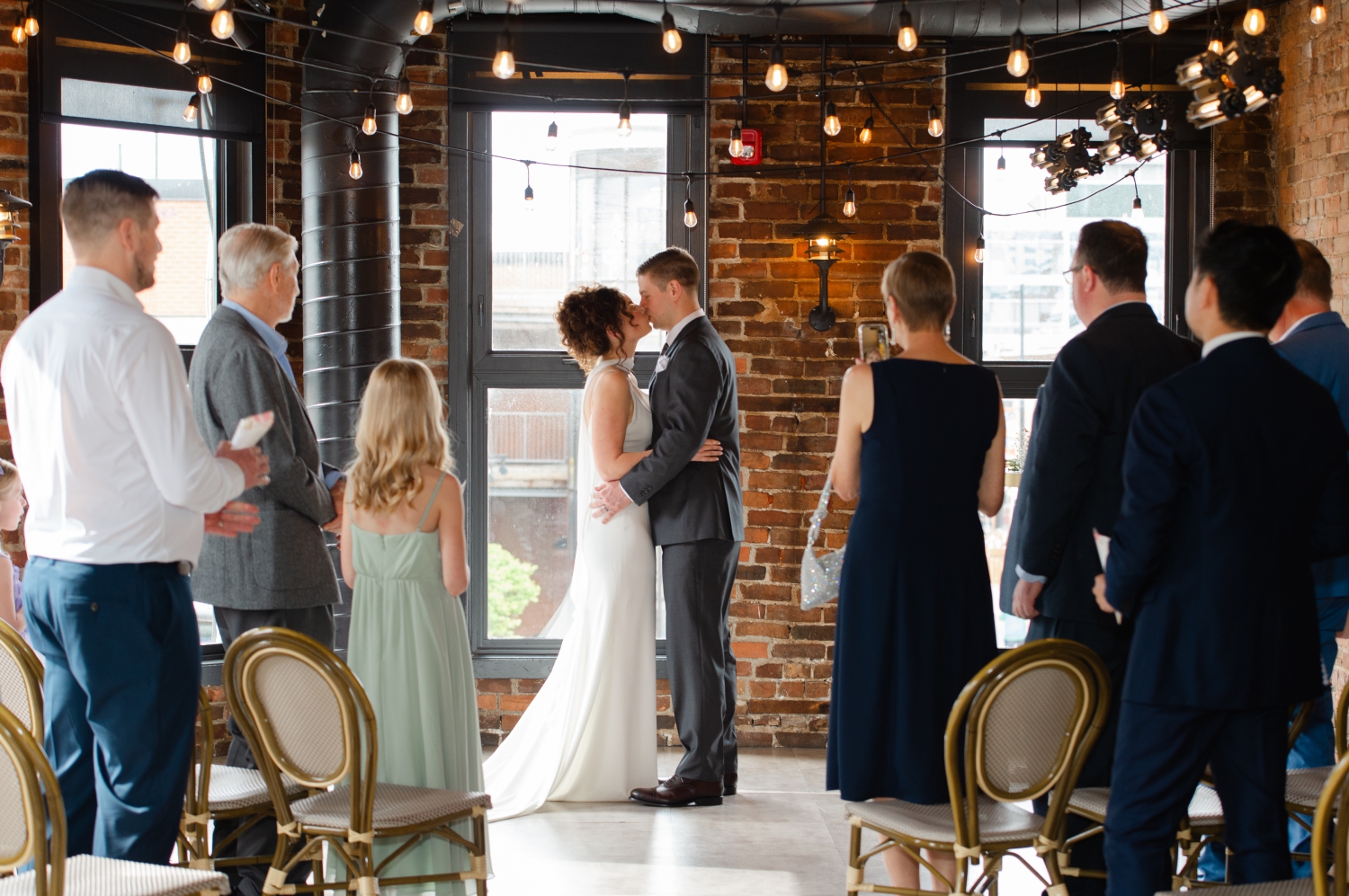 a bride and groom kissing at the end of their Starling Ottawa wedding ceremony while their guests look on and clap. Captured by JEMMAN Photography